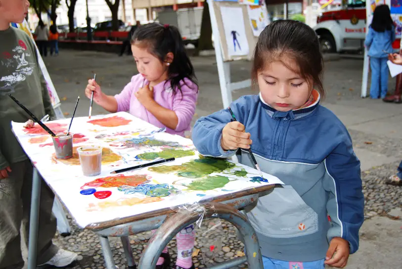 Little girls painting on white canvas using water color and brushes.