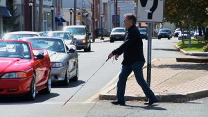 A blind man crossing the street with help of a stick unaware of the traffic on the street