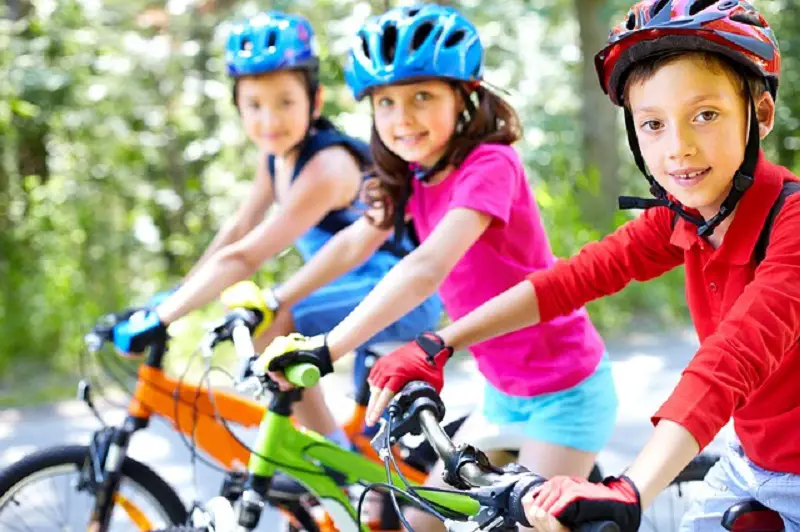 Children are riding bicycle and smiling at the camera.