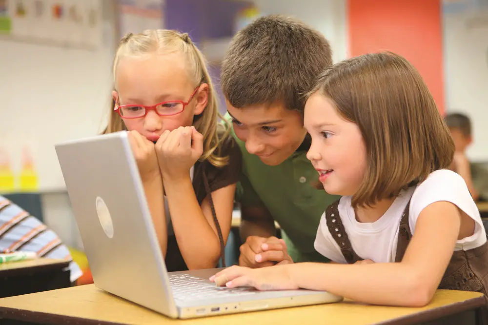 Children using laptop and smiling.